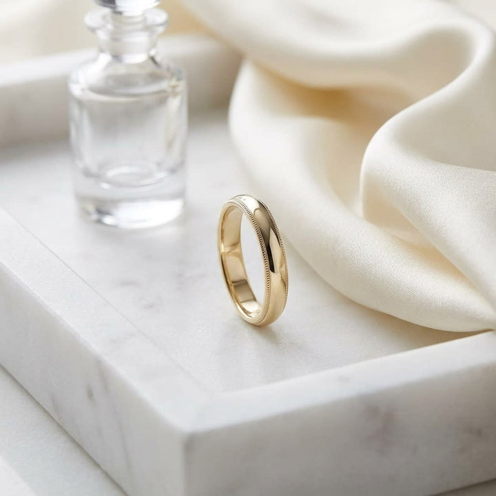 4mm Slightly Domed Traditional Oval Milgrain Wedding Band in 18K Yellow Gold, on marble vanity tray with silk