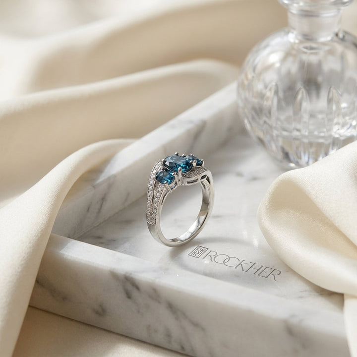 London Blue Topaz Three Stone Swirl Ring in 14k White Gold 0.13ctw, on marble vanity tray with silk