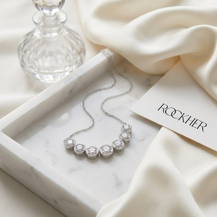 Diamond 7-stone Round Bezel Graduated Necklace With Millgrained Edging in 14K White Gold, on marble vanity tray with silk