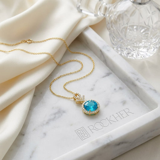 Swiss Blue Topaz Halo Pendant in 14K Yellow Gold, on marble vanity tray with silk