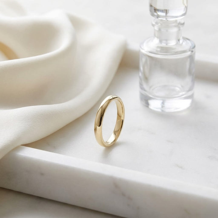 2.5mm Slightly Domed Traditional Oval Wedding Band in 14K Yellow Gold, on marble vanity tray with silk
