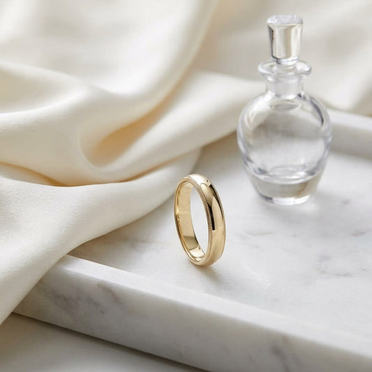 4mm Slightly Domed Traditional Oval Milgrain Wedding Band in 14K Yellow Gold, on marble vanity tray with silk