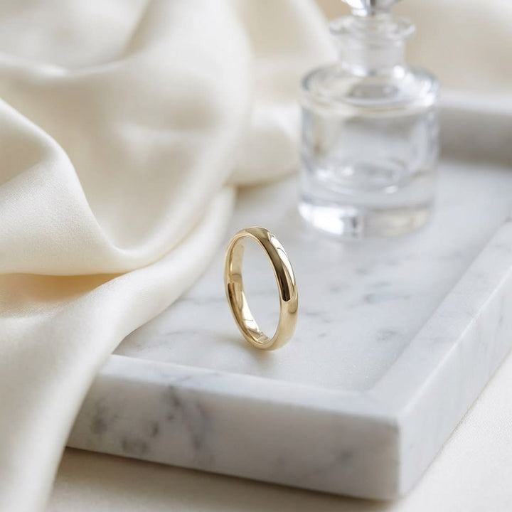 2.5mm Slightly Domed Comfort-Fit Wedding Band in 14K Yellow Gold, on marble vanity tray with silk