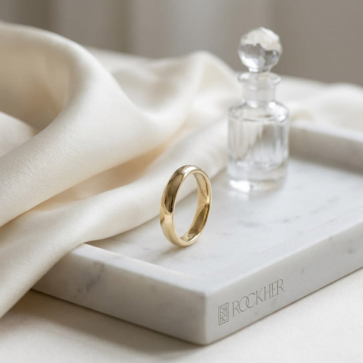 4mm Slightly Domed Comfort-Fit Wedding Band in 14K Yellow Gold, on marble vanity tray with silk