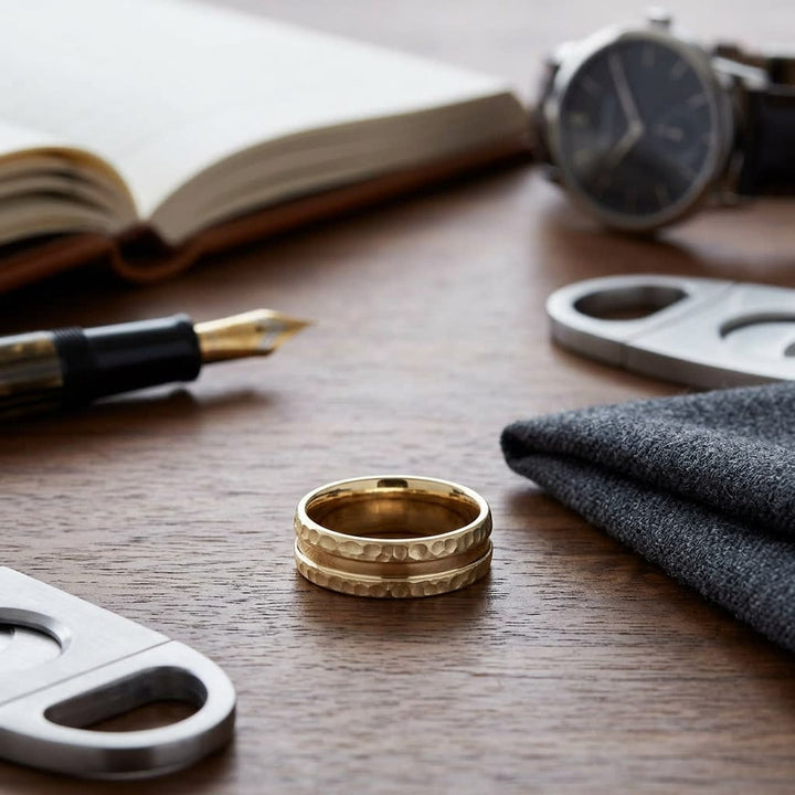 7.5mm Hammered Finish Carved Wedding Band in 14K Yellow Gold, on walnut surface with pocket square