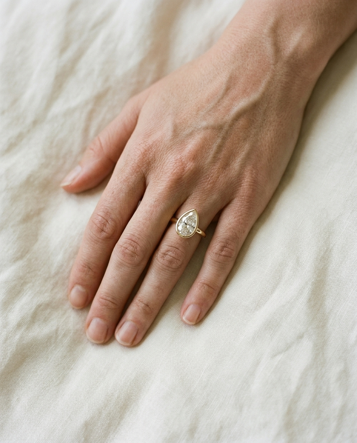 The Agnes Select bezel solitaire briolette engagement ring in 18k yellow gold — top down hand — RockHer