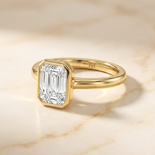 The Agnes Select bezel solitaire emerald cut engagement ring in 18k yellow gold — alt-angle hero — RockHer
