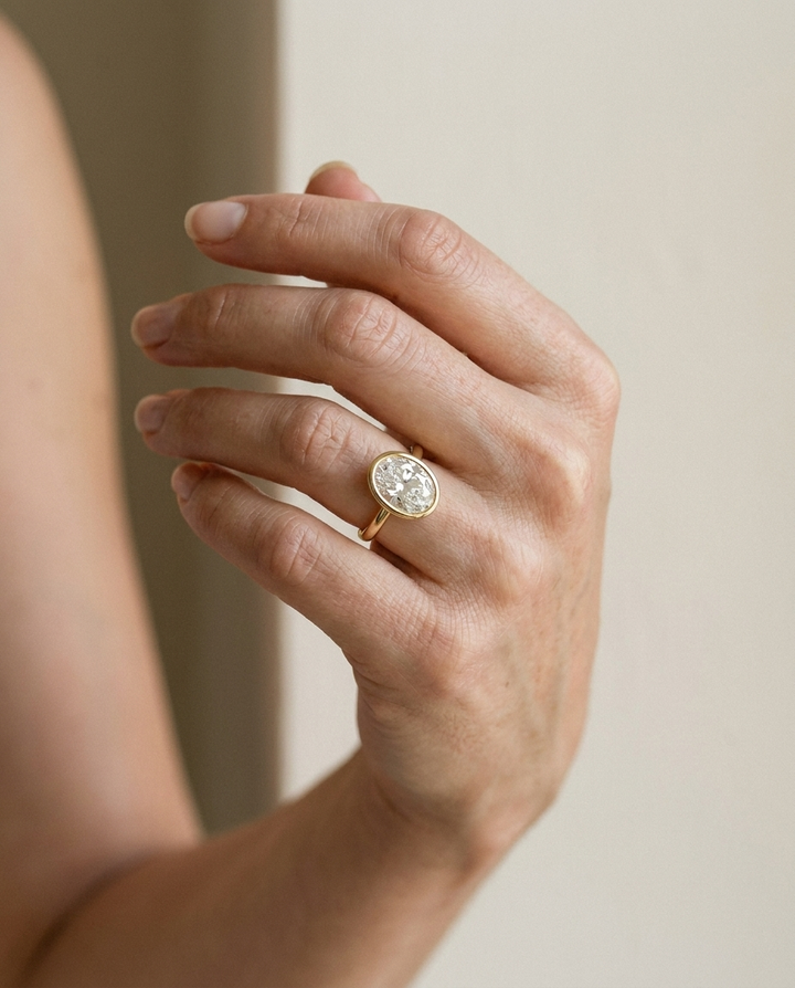 The Agnes Select bezel solitaire oval engagement ring in 18k yellow gold — on hand — RockHer