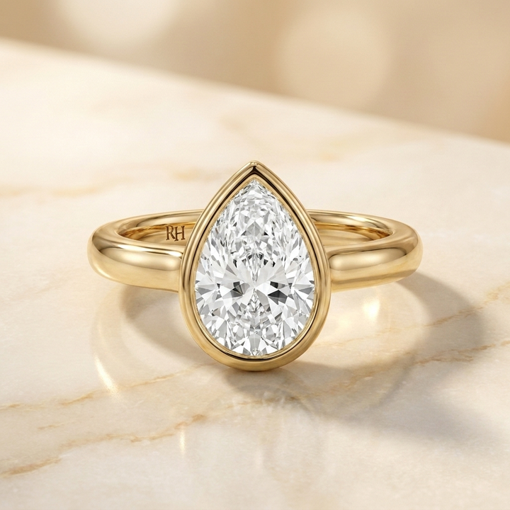 The Agnes Select bezel solitaire pear engagement ring in 18k yellow gold — front view — RockHer