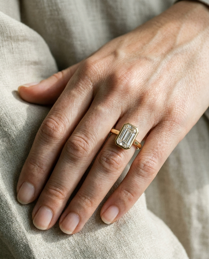 The Agnes Select bezel solitaire tapered baguette engagement ring in 18k yellow gold — on hand — RockHer