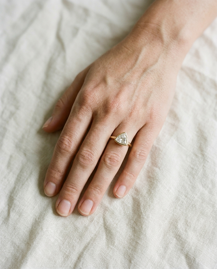 The Agnes Select bezel solitaire trillion engagement ring in 18k yellow gold — top down hand — RockHer